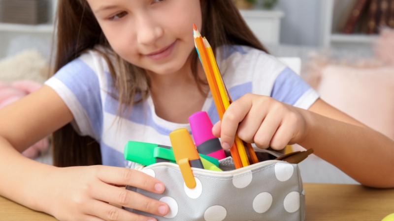 Bambina con astuccio aperto e matite in mano